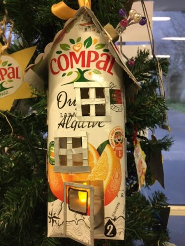 Casinha elaborada com embalagens de Compal, colocada na árvore de Natal. De destacar o pormenor da luz colocada na casinha.